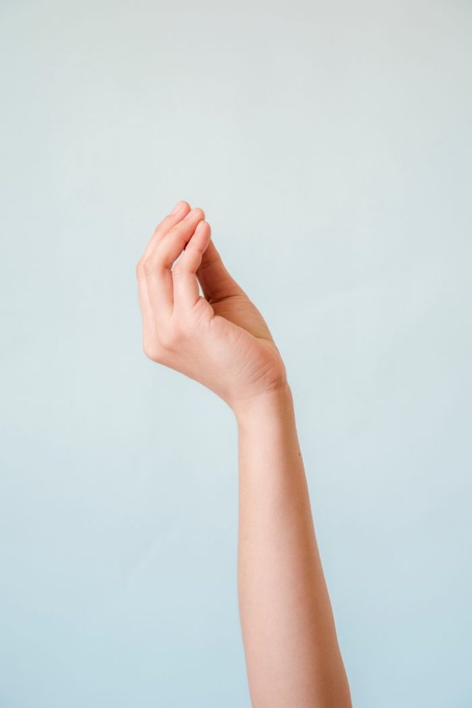 Close-up of a hand making a gesture on a soft blue background, simple and gentle.
