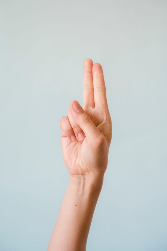 Close-up of a hand making a peace sign against a light blue background.