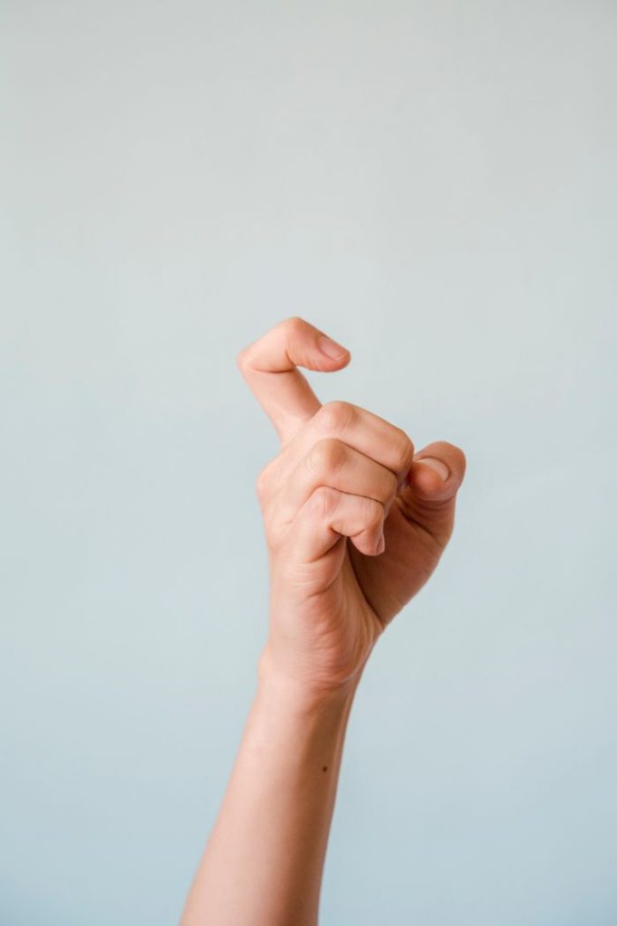 Close-up of a hand making a gesture against a soft blue background.