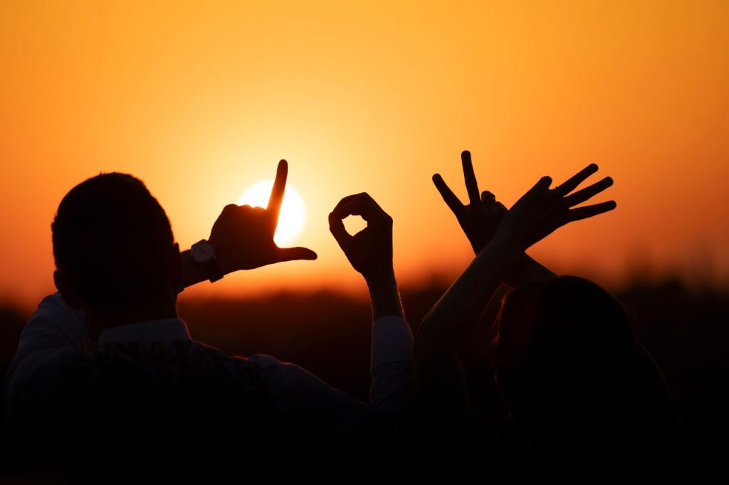 Silhouette of individuals spelling LOVE with hands against a sunset backdrop.