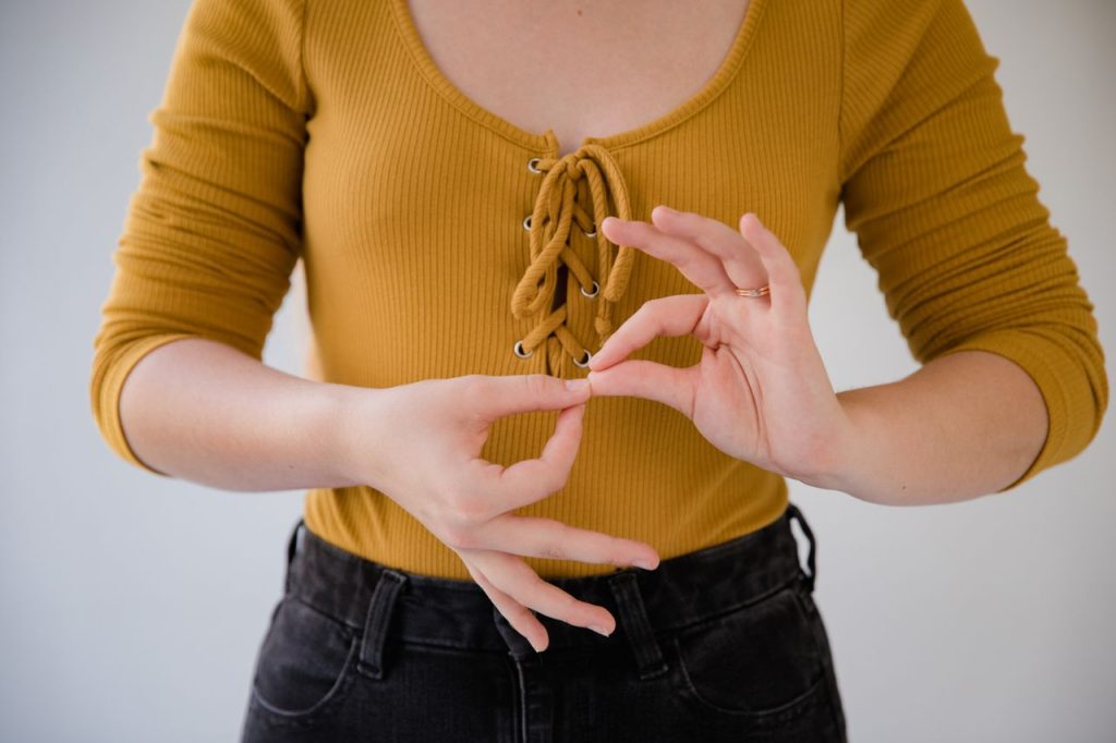 Close-up of a woman in a yellow top using hand gestures presumably for communication.